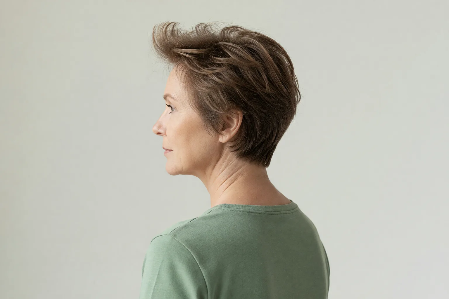 Three-quarter back view of a woman in her late 50s with a short layered crop that adds lift at the crown