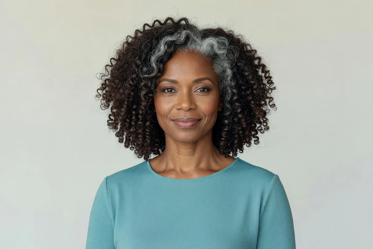 Woman around 54 with a rounded shoulder-length cut of natural curly hair with silver strands at the temples