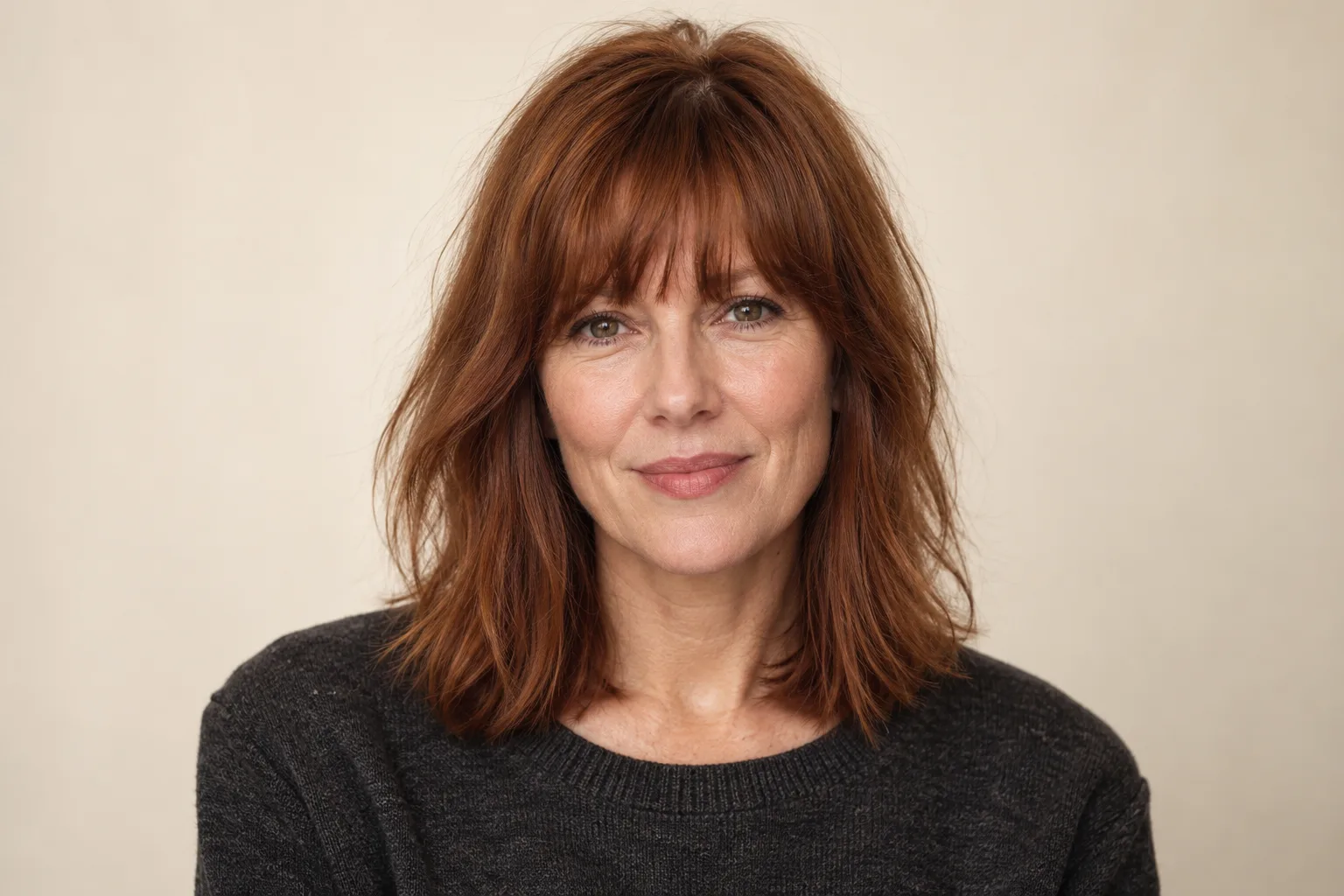 Soft full fringe crossing the forehead above collarbone-length auburn hair